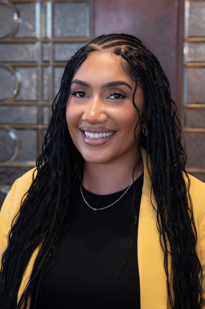 Professional headshot of Marlika Harris wearing a yellow blazer over a black top, smiling against a softly blurred indoor background.