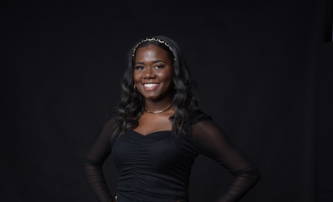 Studio portrait of Tori Henry in a black dress, framed from the head through the upper torso against a dark background.